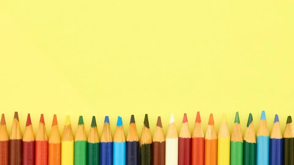 Une rangée de crayons de couleur alignés au bas d'un fond jaune.