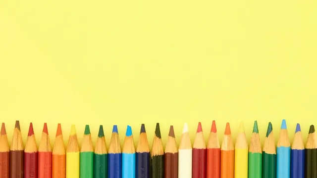 Une rangée de crayons de couleur alignés au bas d'un fond jaune.